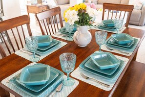 Un tavolo da pranzo apparecchiato con bicchieri e piatti color acquamarina, un vaso bianco con fiori e un tavolo da pranzo in legno.
