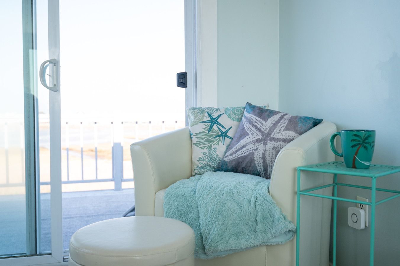 A room with a white chair, a teal mug, and a glass table.