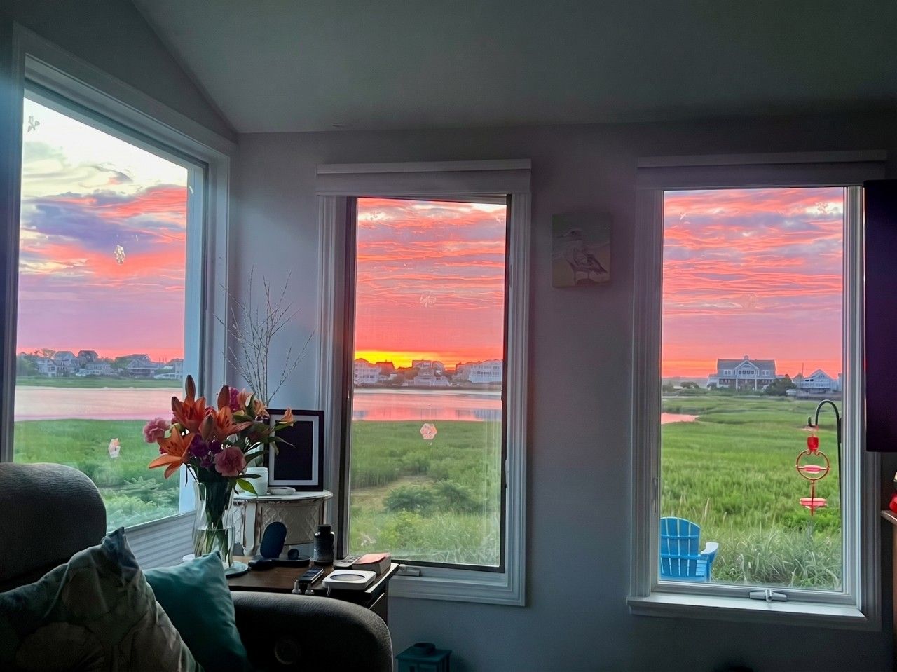 Een kamer met een bureau, een stoel en uitzicht op een zonsondergang boven het water.