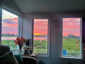 A room with a desk, a chair, and a view of a sunset over a body of water.