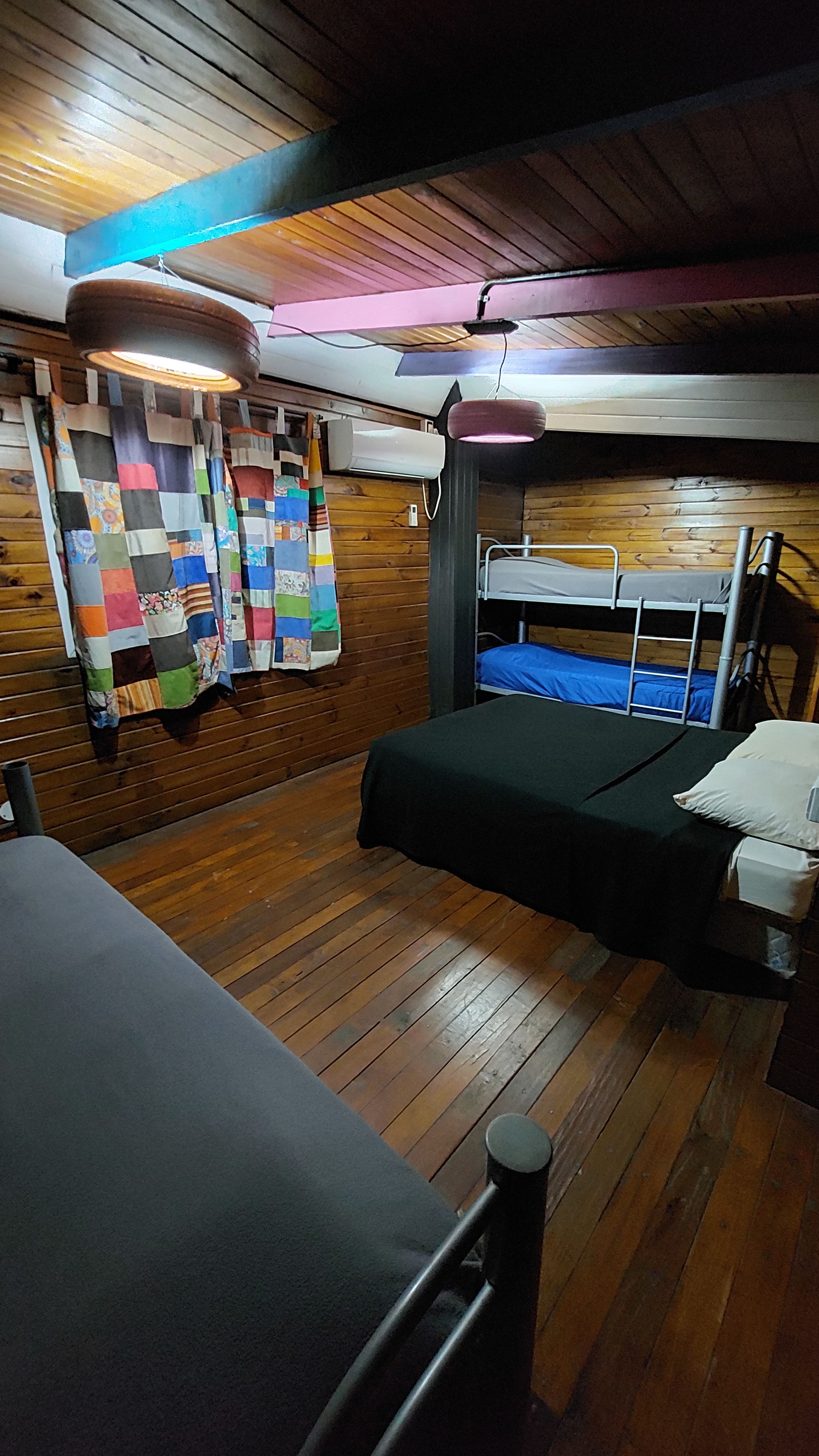 A room with wooden flooring, a bunk bed, a colorful quilt, and a hanging light fixture.