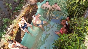 A group of people in a natural pool surrounded by rocks and plants.