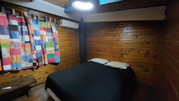 A room with wooden walls, a bed with a black bedspread, a white pillow, and a colorful quilt hanging on the wall.