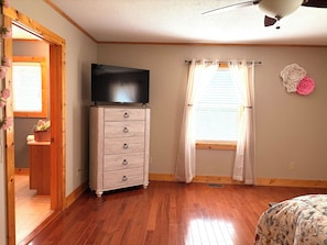 A room with a wooden dresser, a flat-screen TV, a window with sheer curtains, and a ceiling fan. -  Peaceful Lenoir Retreat - 3BR/2BA- Minutes from Morganton & 30 mins to Boone (Lenoir)
