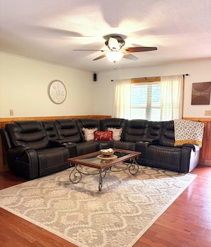 A living room with a sectional sofa, a glass coffee table, and a ceiling fan. -  Peaceful Lenoir Retreat - 3BR/2BA- Minutes from Morganton & 30 mins to Boone (Lenoir)