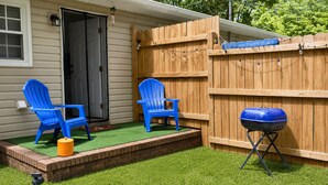 Ein Garten mit zwei blauen Stühlen, einem Grill und einem Holzzaun.