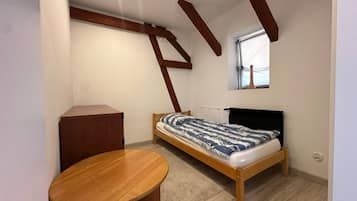 Un dormitorio pequeño con una cama individual, una mesa de madera y una ventana.