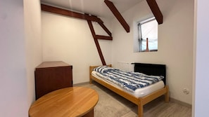 A small bedroom with a single bed, a wooden table, and a window.