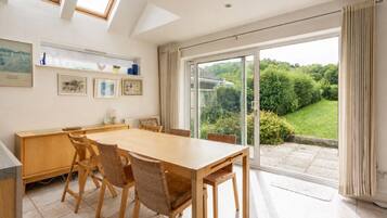 A dining area with a large table and chairs, a wooden cabinet, and a view of a garden through a sliding glass door.