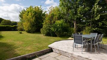 Une terrasse avec une table et des chaises, entourée d’une pelouse et d’arbres.