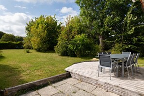 Une terrasse avec une table et des chaises, entourée d’une pelouse et d’arbres.