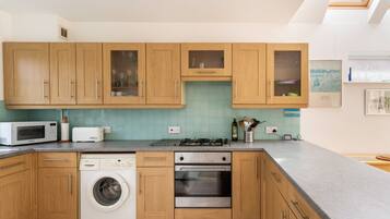 Une cuisine moderne avec des meubles en bois, un lave-linge, un four à micro-ondes et une cuisinière à gaz.