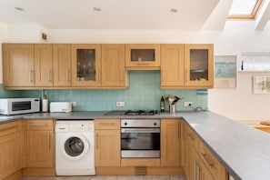 Une cuisine moderne avec des meubles en bois, un lave-linge, un four à micro-ondes et une cuisinière à gaz.