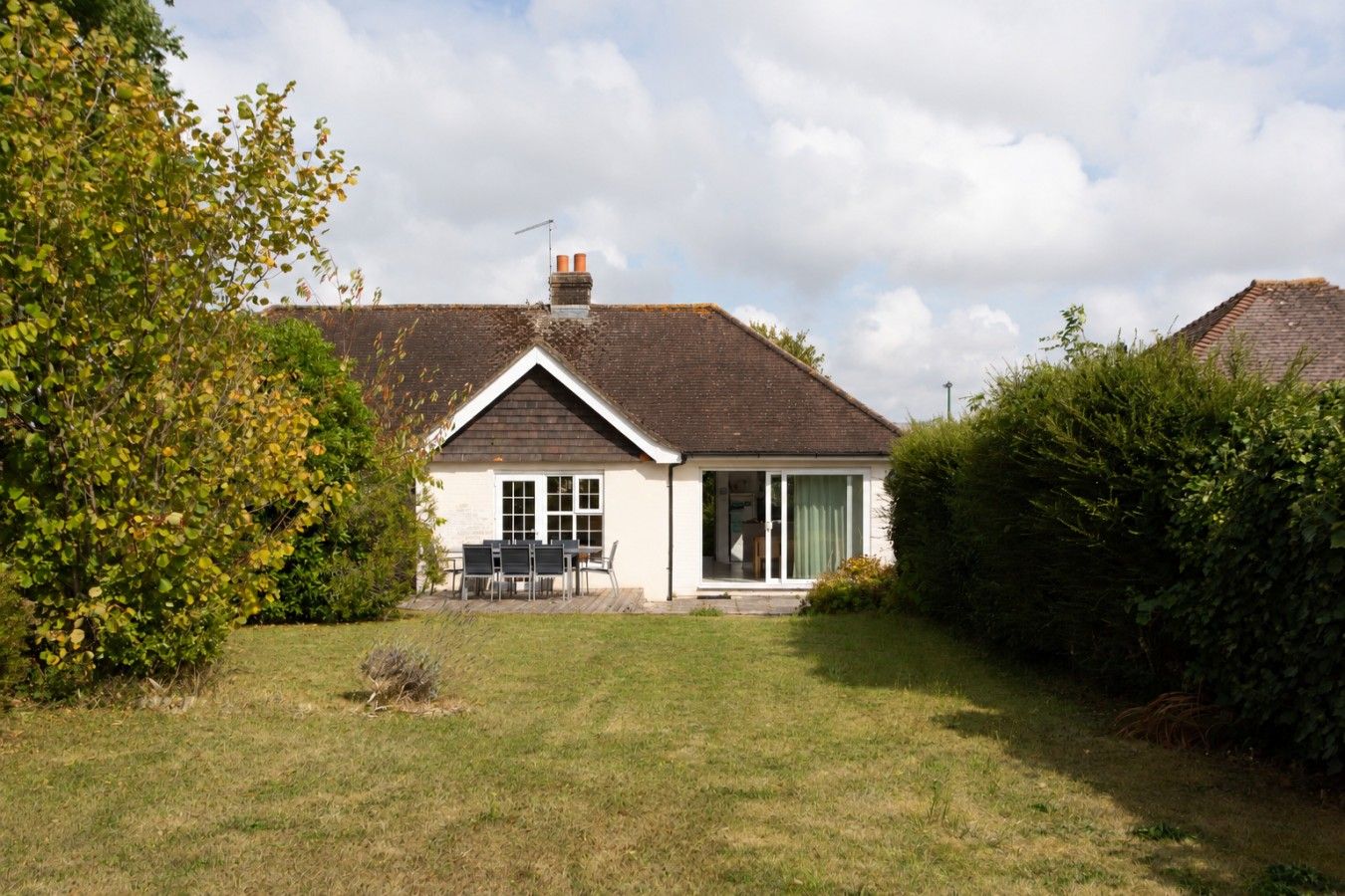 A single-story house with a sloped roof, a chimney, and a front porch with a table and chairs.