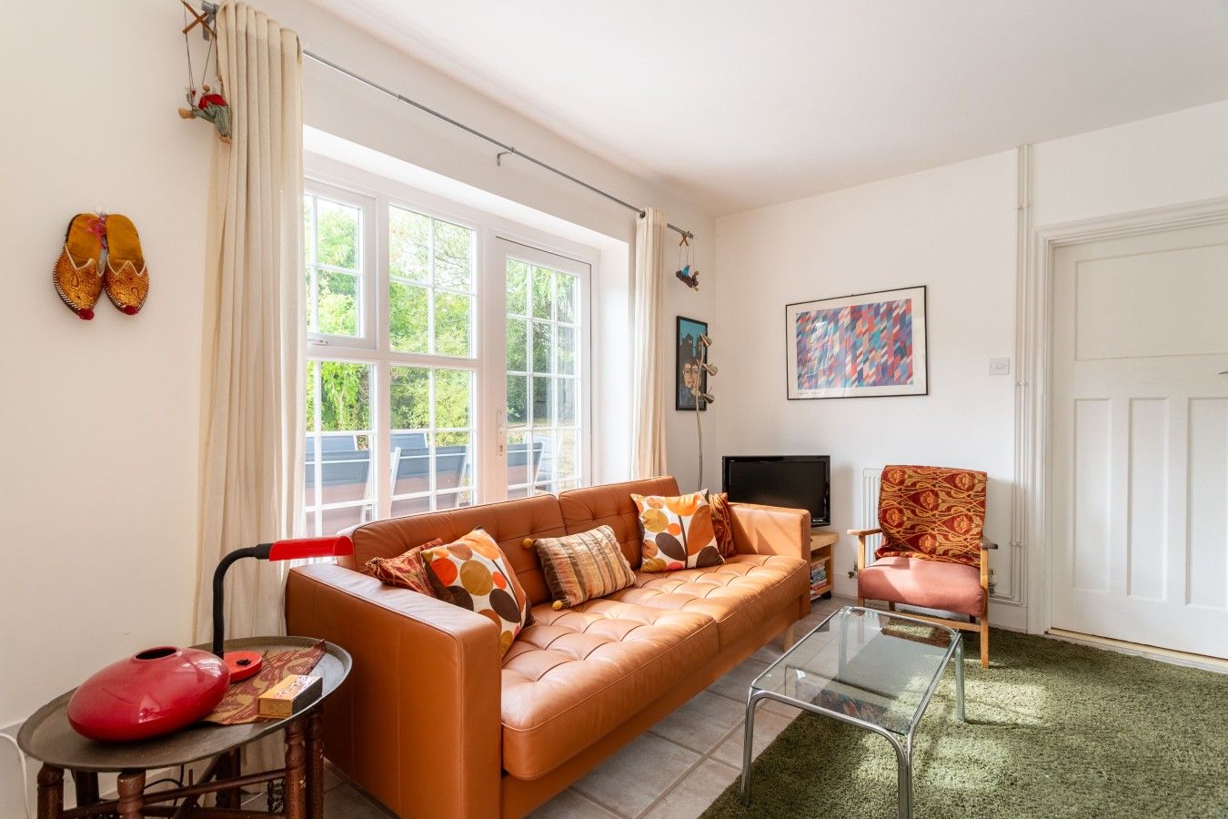 A living room with a leather sofa, a glass coffee table, a red chair, a television, and a door.
