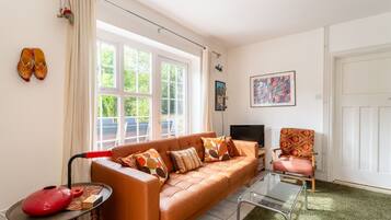 A living room with a leather sofa, a glass coffee table, a red chair, a television, and a door.