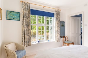 Un dormitorio con una cama grande, una ventana con cortinas, una silla y una puerta que da a otra habitación.