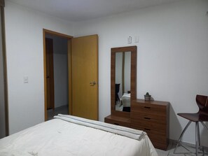 A bedroom with a bed, a wooden dresser, a mirror, and a chair. - Casa Buda Tonalá Downtown (Tonalá)