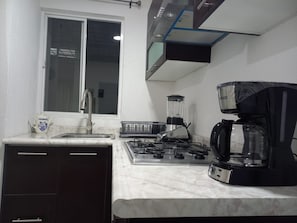 Eine Küche mit Gaskochfeld, Kaffeemaschine, Mixer und einem Fenster mit Aussicht.