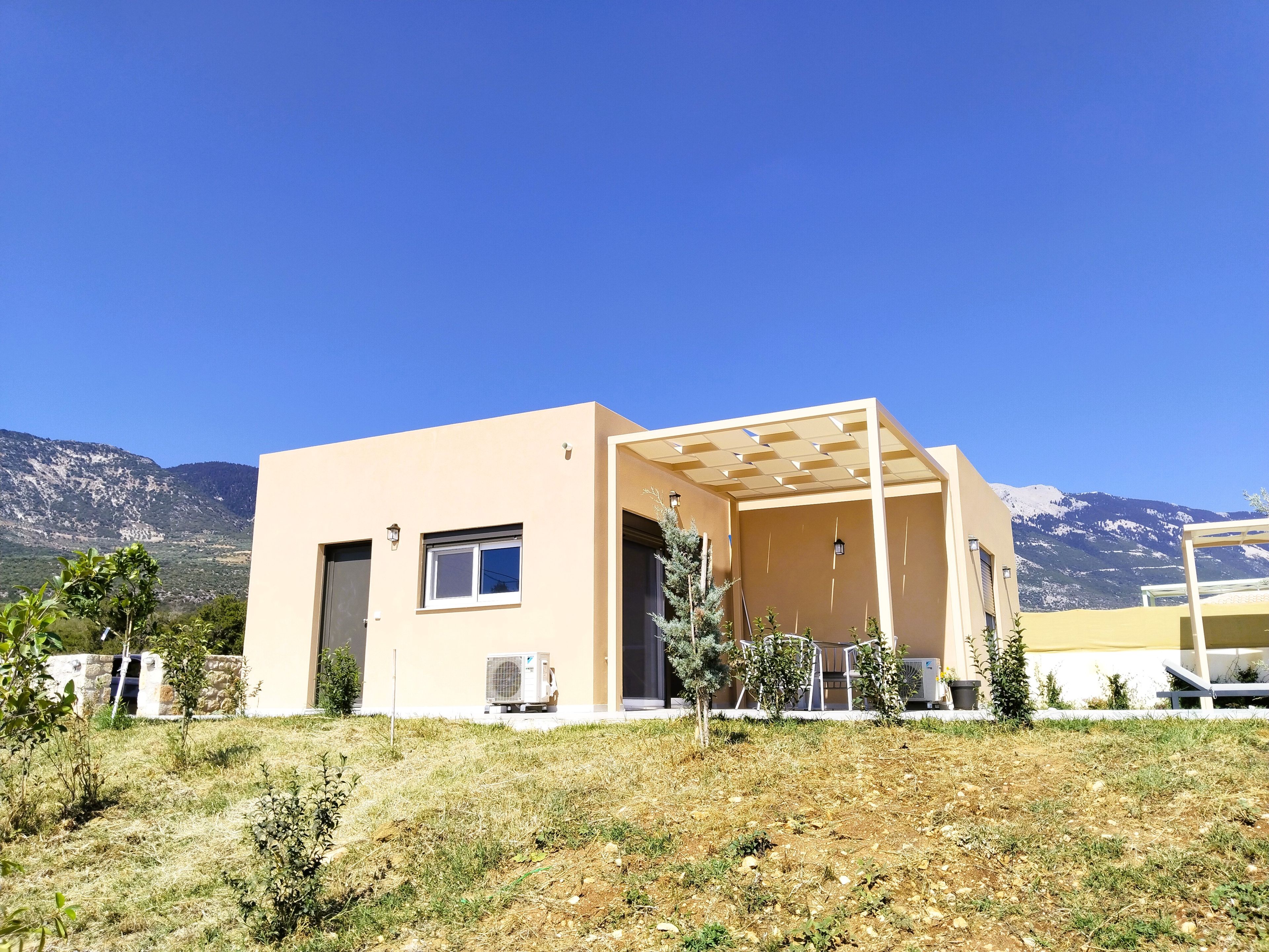 A modern building with a flat roof, a covered outdoor area, and a view of mountains in the background.