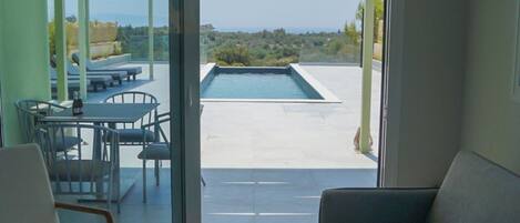 Un salon moderne avec un canapé, une table et une vue sur une piscine extérieure et un mobilier de jardin.