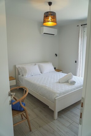 Ein Schlafzimmer mit einem Bett, einem Nachttisch, einem Sessel, einer Hängelampe und einem Fenster mit Vorhängen.