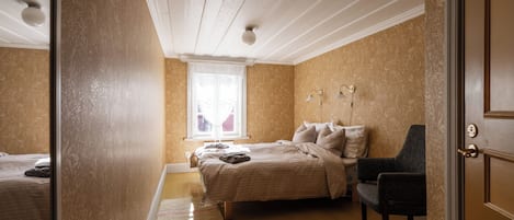 A bedroom with a bed, a chair, a window with curtains, and a door.