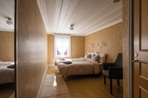 A bedroom with a bed, a chair, a window with curtains, and a door. - Gården (Korsholm)