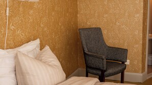 A hotel room with a bed, a chair, and a wall with floral wallpaper.