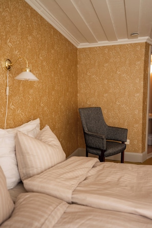 A hotel room with a bed, a chair, and a wall with floral wallpaper. - Gården (Korsholm)
