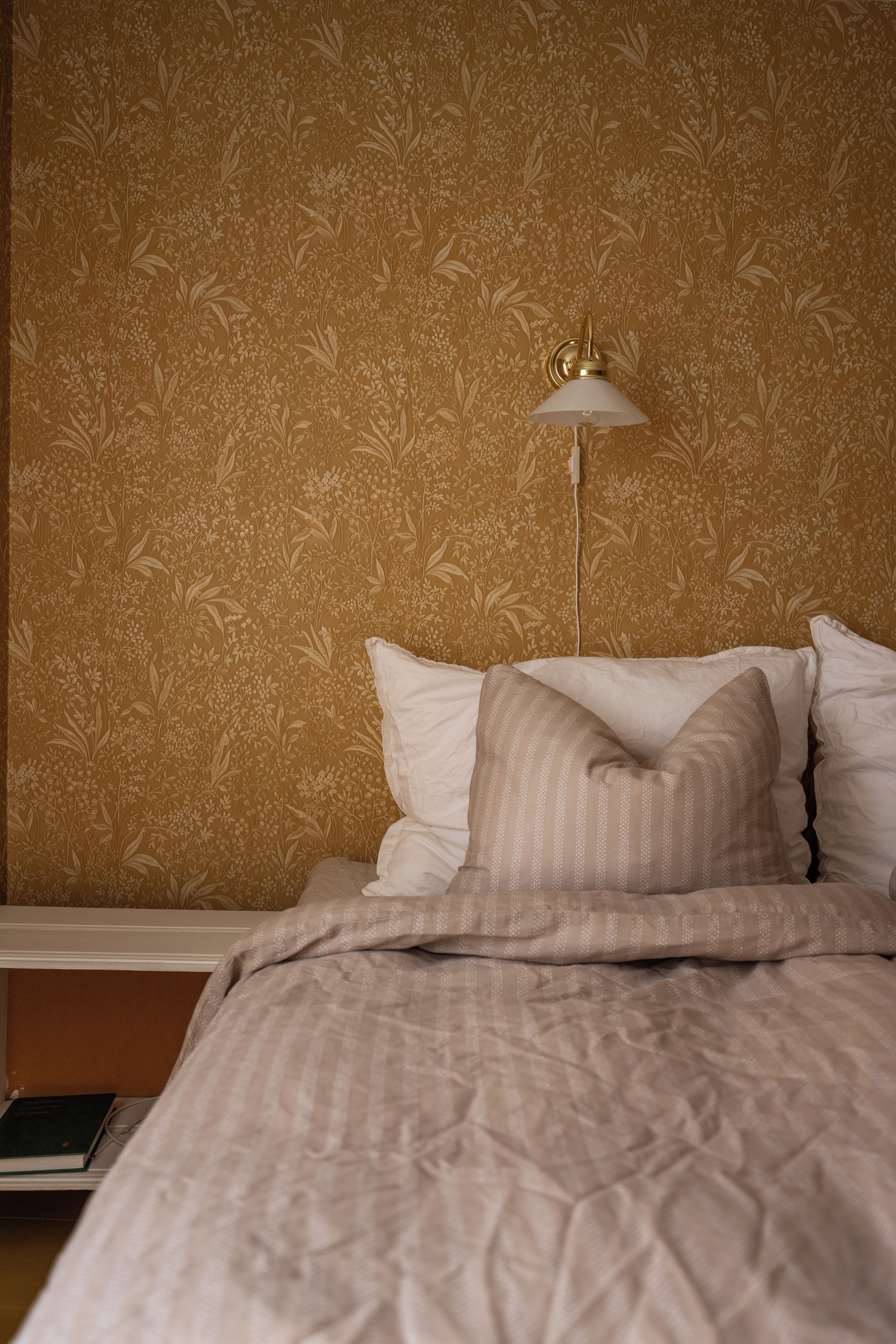 Quarto com papel de parede estampado, luminária de cabeceira e cama com almofadas.