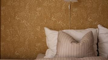 Quarto com papel de parede estampado, luminária de cabeceira e cama com almofadas.
