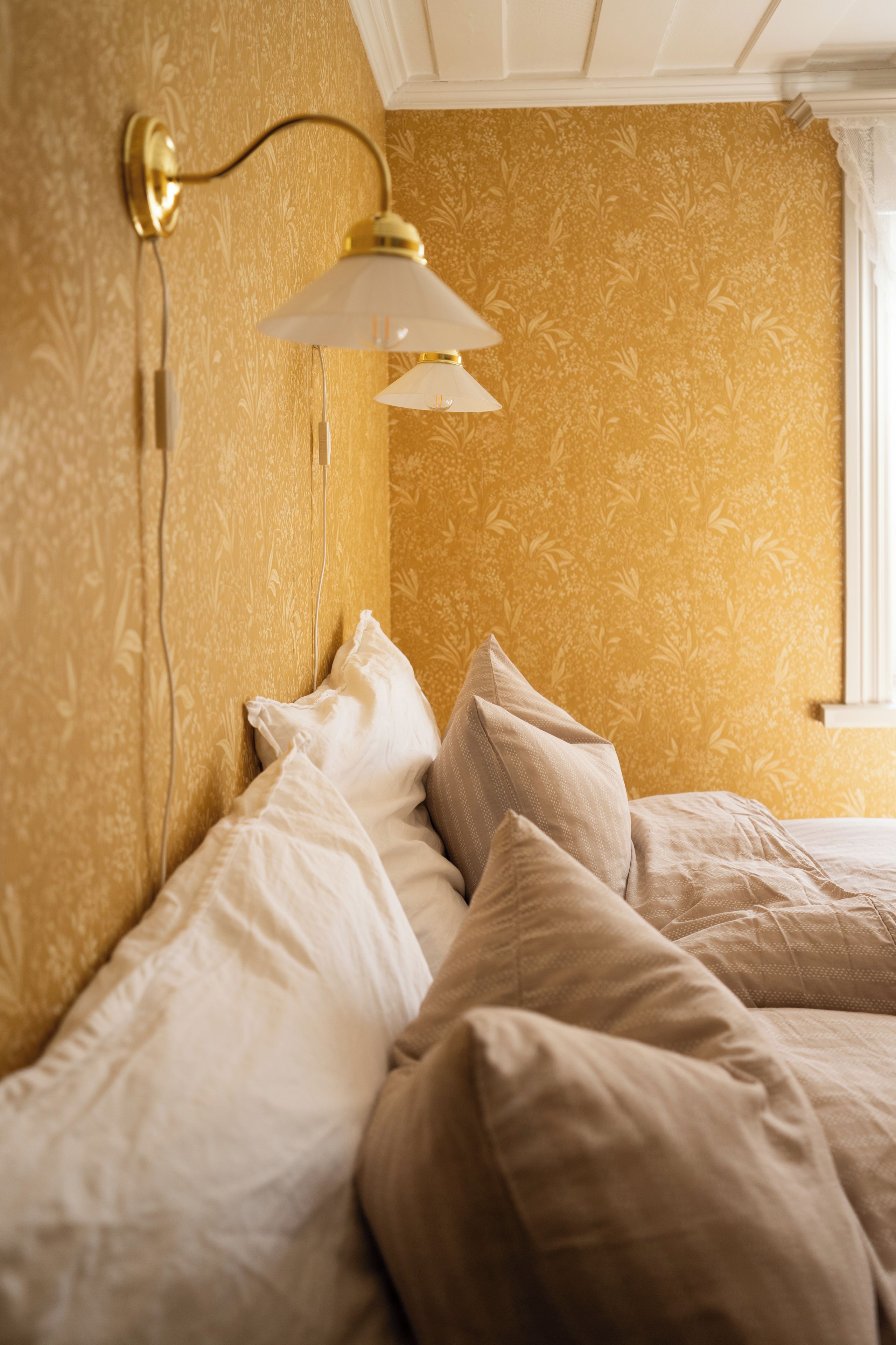 Ein Schlafzimmer mit einem Bett, Kissen, einer Wandlampe und einem Fenster.