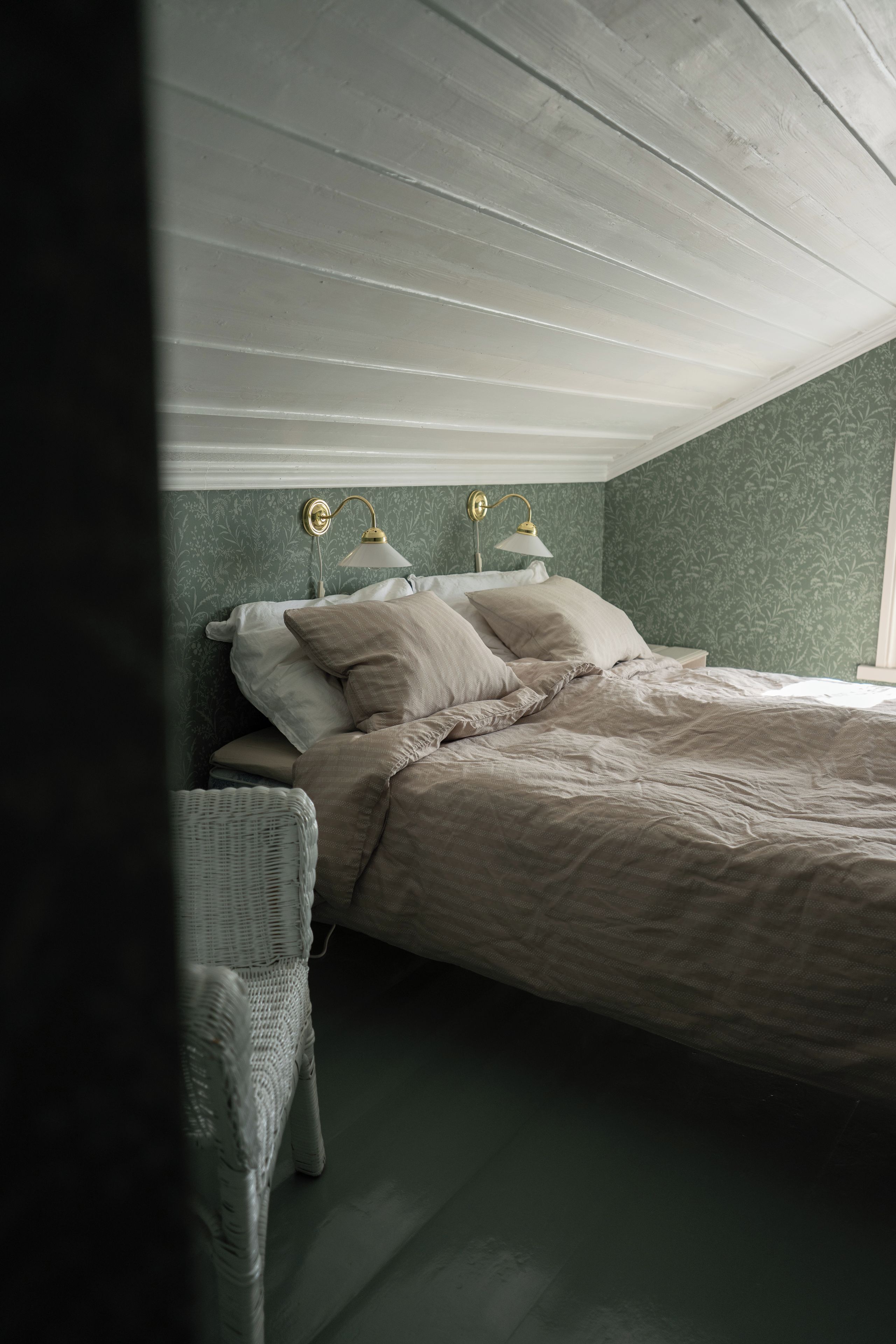 Een slaapkamer met een bed, twee bedlampen, een nachtkastje en een rieten stoel.