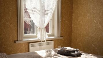 Quarto com cama, janela com cortina leve e radiador.