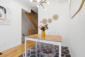 A dining area with a wooden table, clear chairs, a yellow vase with flowers, and a staircase in the background. - Modern 3BR Townhome | 3 Ensuite Bedrooms | 5min to Subway | Steps to Restaurants (Toronto)