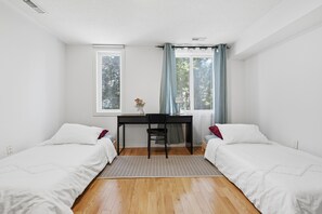 Ein Zimmer mit zwei Einzelbetten, einem Schreibtisch mit Stuhl, einem Fenster mit Vorhängen und einer Heizung.