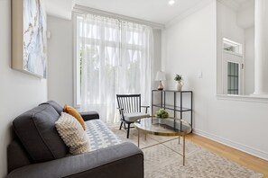 Ein modernes Wohnzimmer mit einem grauen Sofa, einem runden Glastisch, einem schwarzen Sessel und einem weißen Teppich.