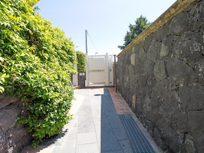 Ein schmaler Pfad, an einer Seite eine Steinmauer und an der anderen ein Metallgitter.