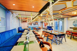 Ein Restaurant mit blauen Sitzecken, orangefarbenen Stühlen und verschiedenen Hängelampen.