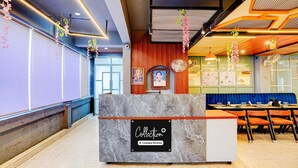 A reception area with a marble counter, a seating area with blue upholstered benches, and a wall with framed artwork. - Collection O Kotdwar Railway Junction (Kotdwāra)