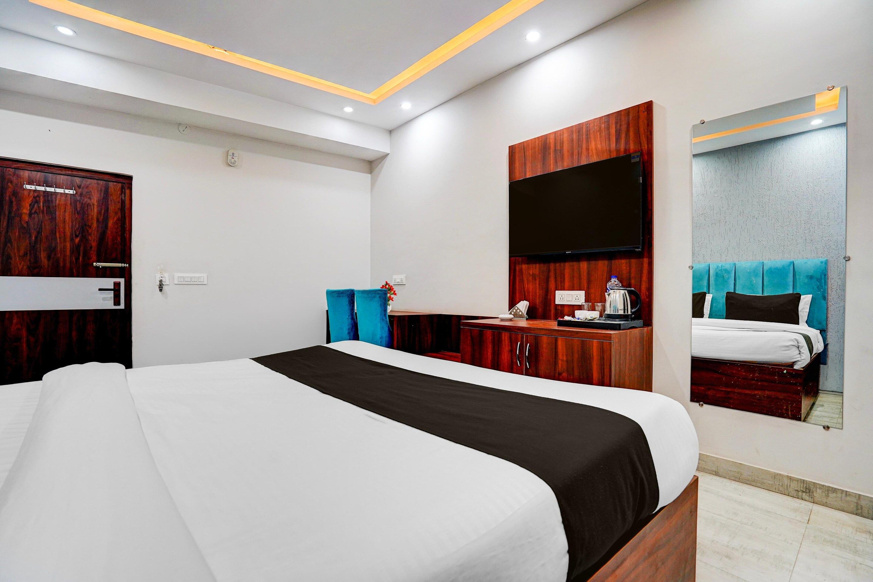 A hotel room with a large bed, a wooden wardrobe, a flat-screen TV, and a mirror.