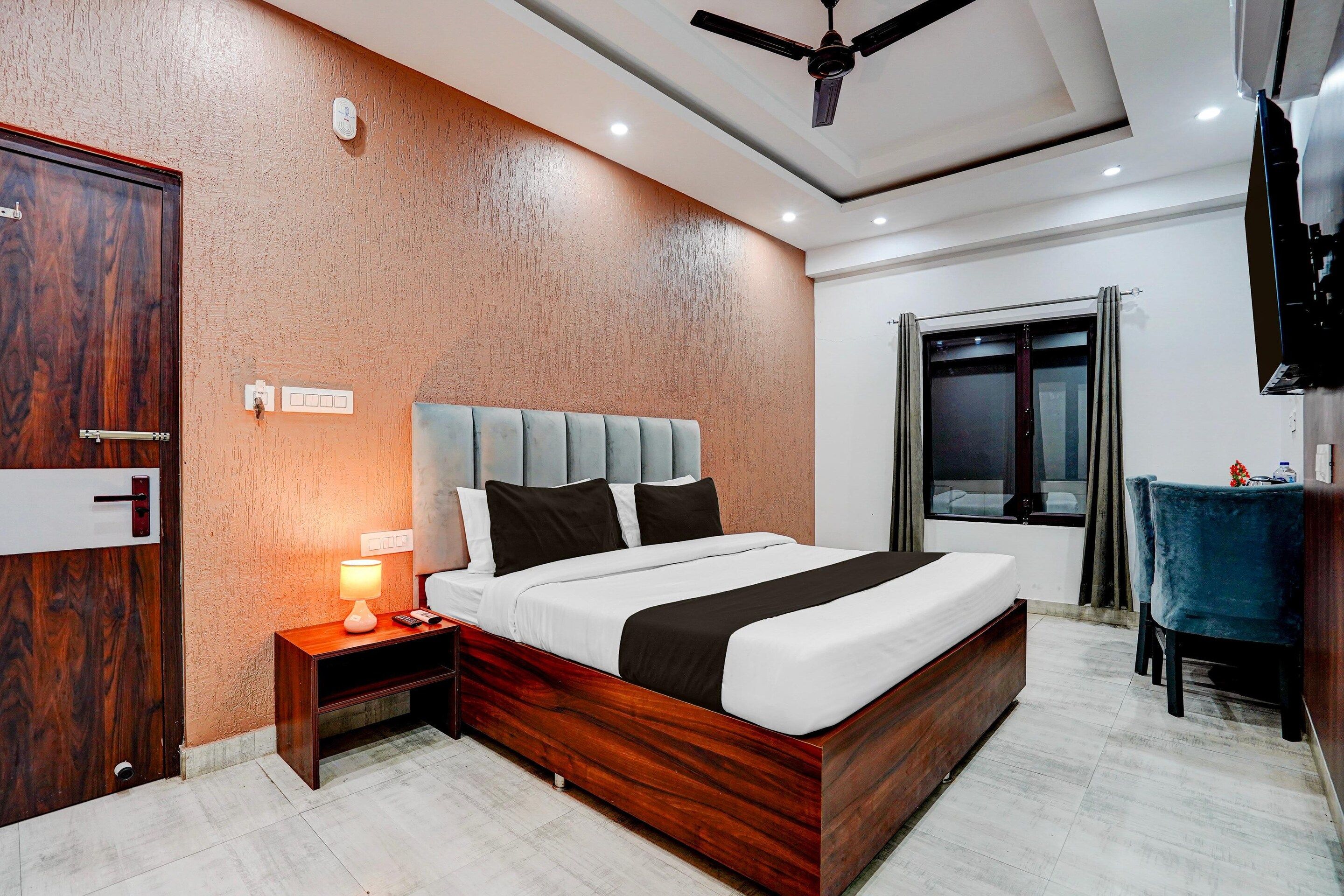 A hotel room with a bed, bedside table, lamp, and a window with curtains.
