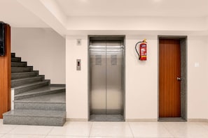 A modern elevator with a digital display, a fire extinguisher mounted on the wall, and a wooden door to the right.