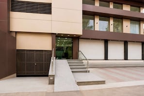 Un edificio de diseño moderno, con una escalera que lleva a una entrada de vidrio, una reja metálica y varias persianas enrollables cerradas.