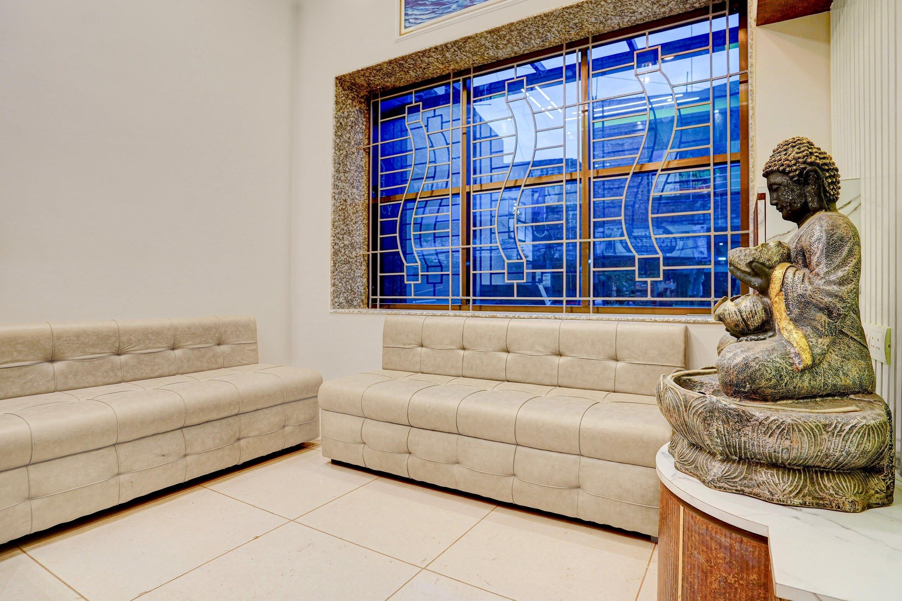 Una habitación con un sofá de color beige, una estatua y un ventanal azul con un diseño geométrico.