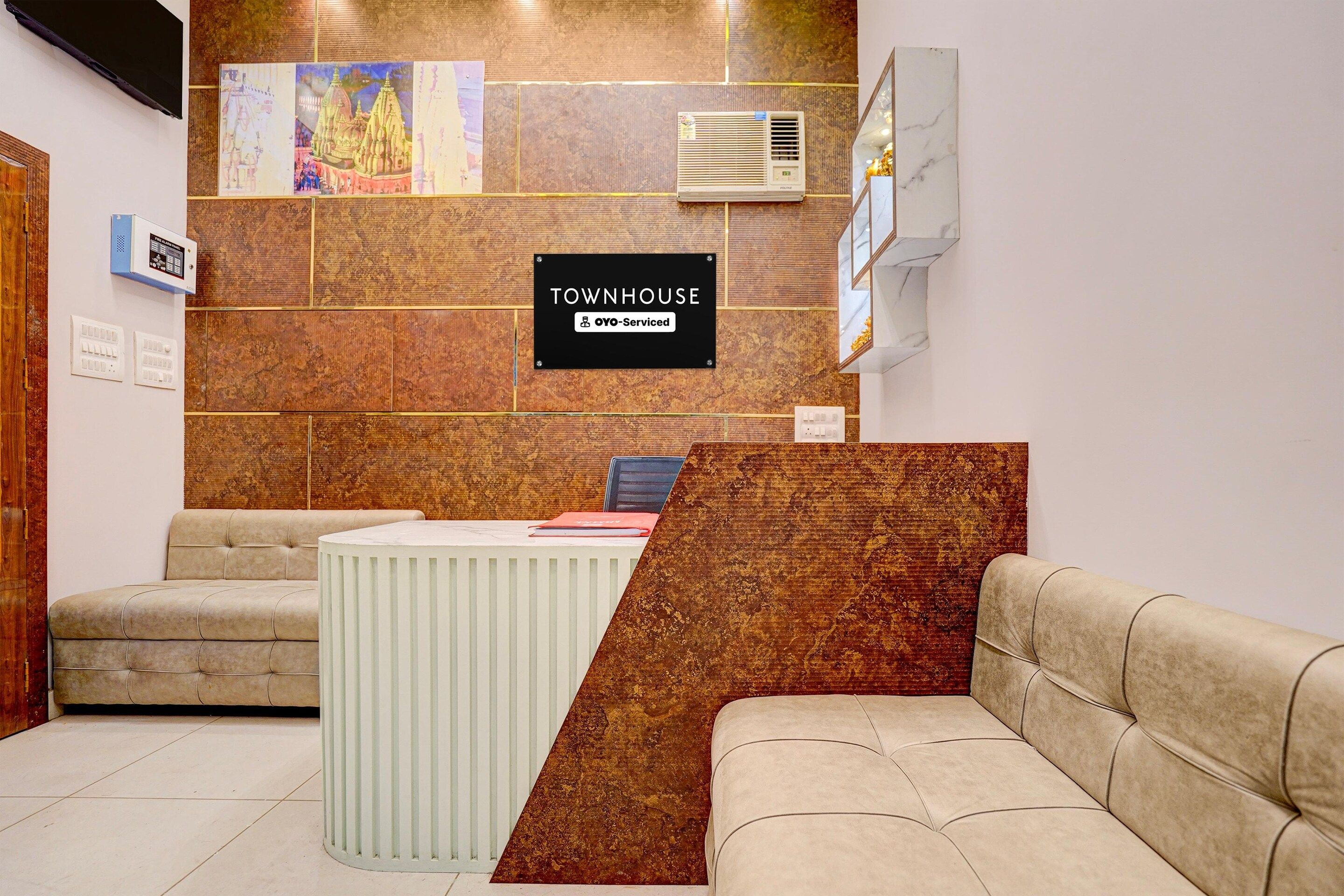 A reception area with a reception desk, two sofas, a bulletin board with artwork, and a sign indicating the property is serviced by OYO.
