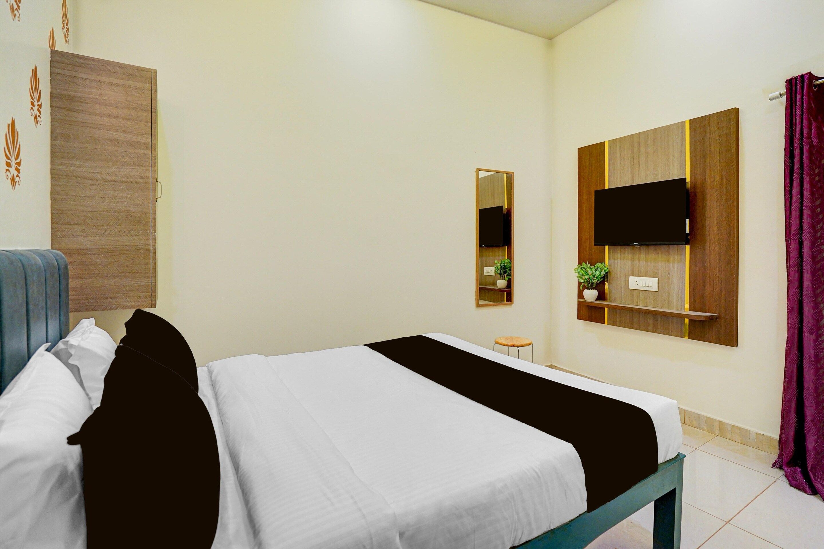 A hotel room with a bed, a television mounted on the wall, a small table, and a potted plant.