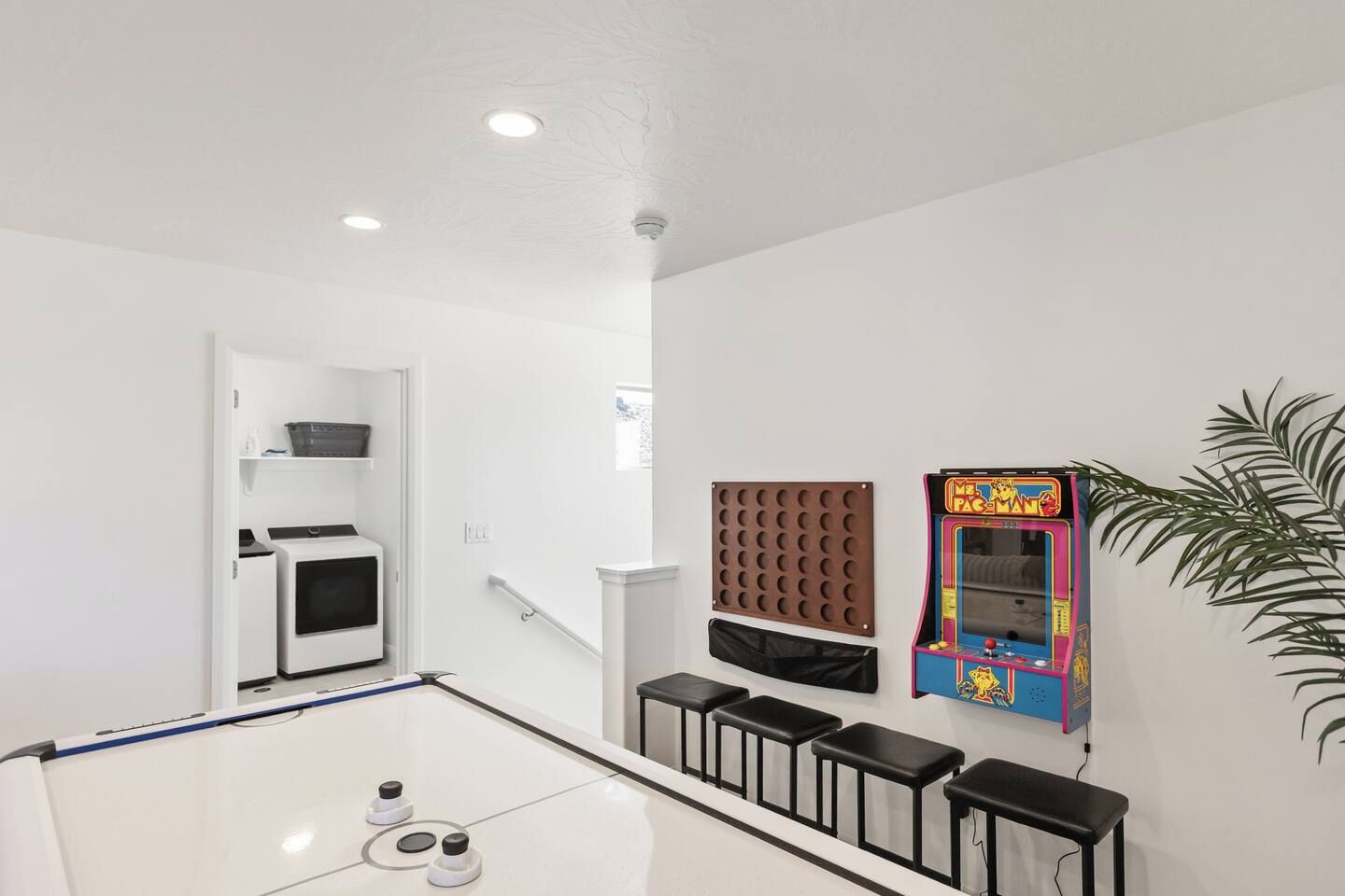 A room with a white ceiling, recessed lighting, a microwave, a small refrigerator, a wall-mounted game machine, and a plant.