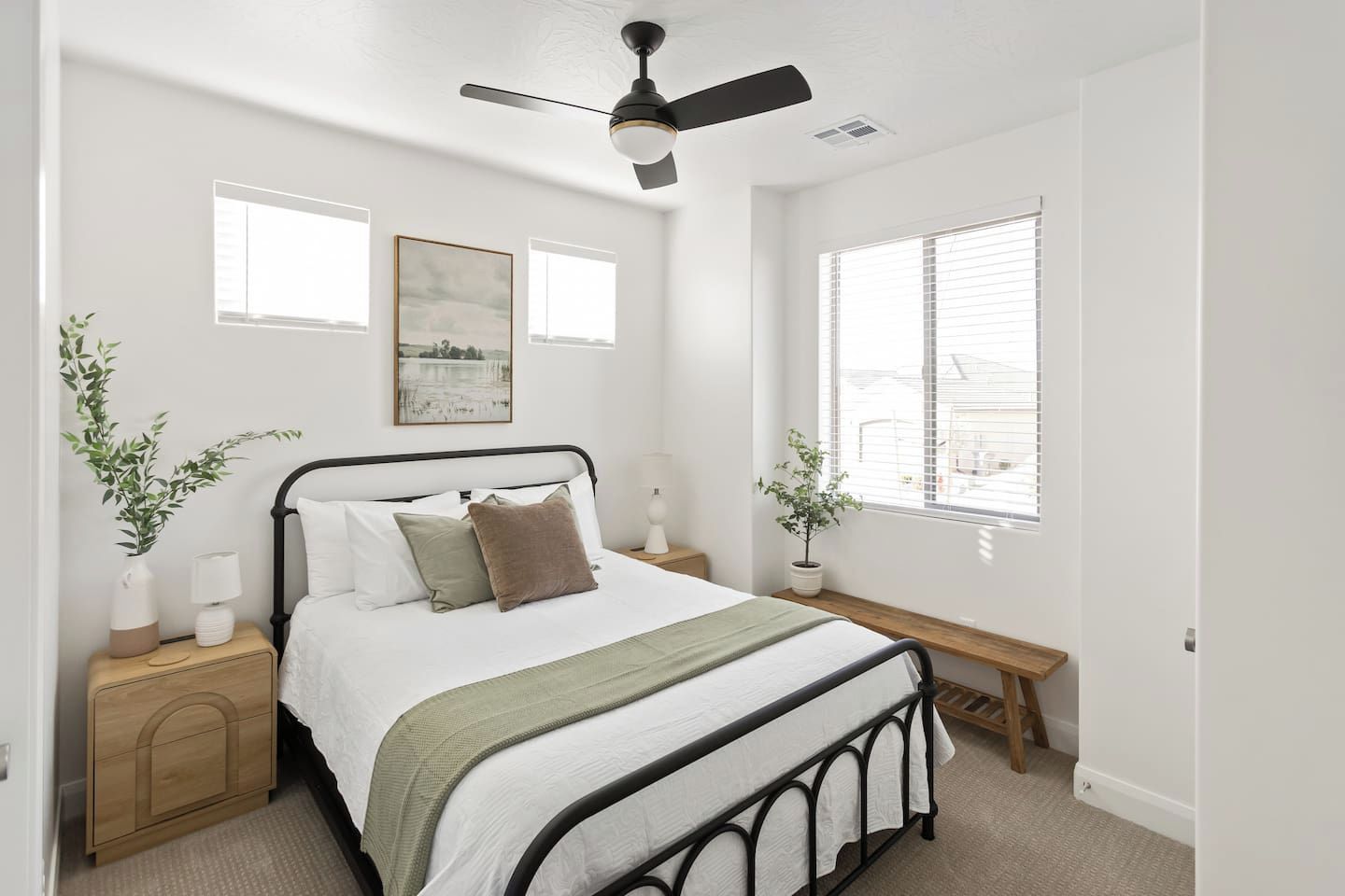 Quarto com cama, mesas de cabeceira, ventoinha no teto, janela com persianas e uma obra de arte na parede.